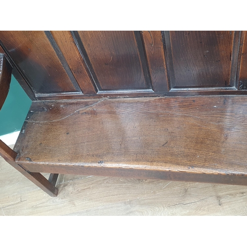 445 - An 18th Century oak Settle with multiple fielded panels to the back, shaped arms on squared supports... 