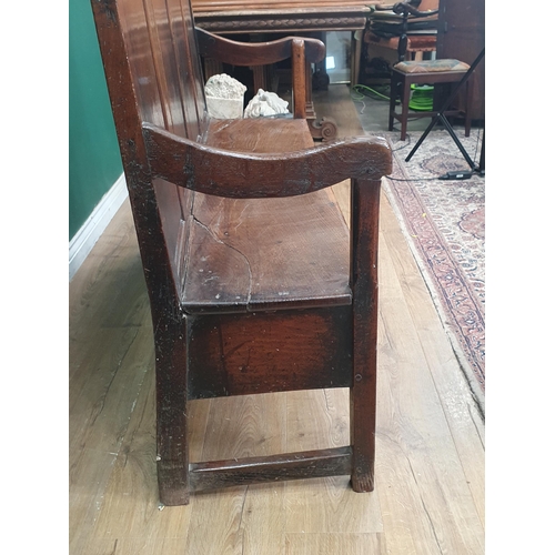 445 - An 18th Century oak Settle with multiple fielded panels to the back, shaped arms on squared supports... 