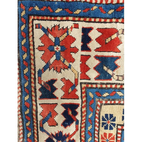 630 - An antique bordered Kazak Rug, the red central field with six guls having latch hook edges, the main... 