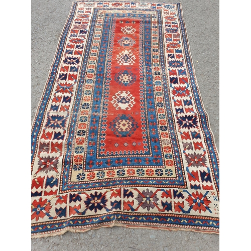 630 - An antique bordered Kazak Rug, the red central field with six guls having latch hook edges, the main... 