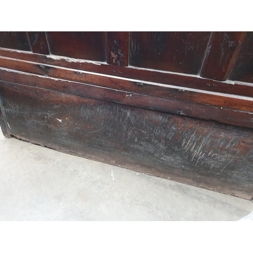 445 - An 18th Century oak Settle with multiple fielded panels to the back, shaped arms on squared supports... 