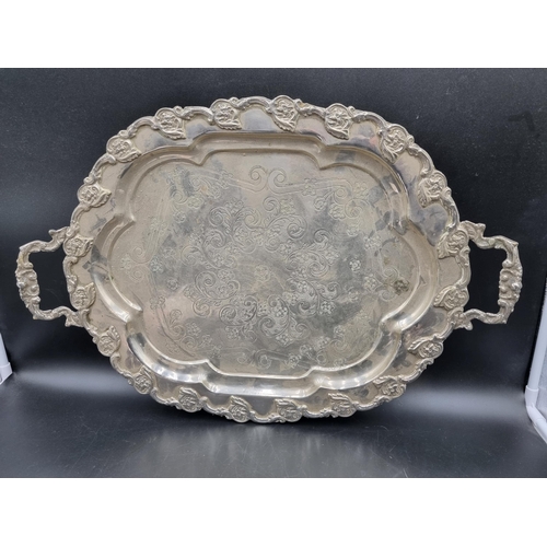 25 - A white metal two handled shaped oval Tea Tray with floral scroll decoration on paw feet, 24in