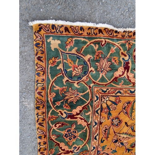 935 - A modern woolen Persian style Rug with trailing floral design on mustard ground within wide green bo... 