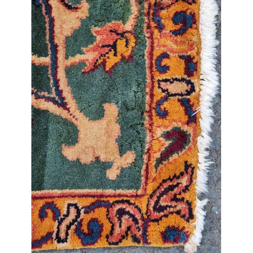 935 - A modern woolen Persian style Rug with trailing floral design on mustard ground within wide green bo... 