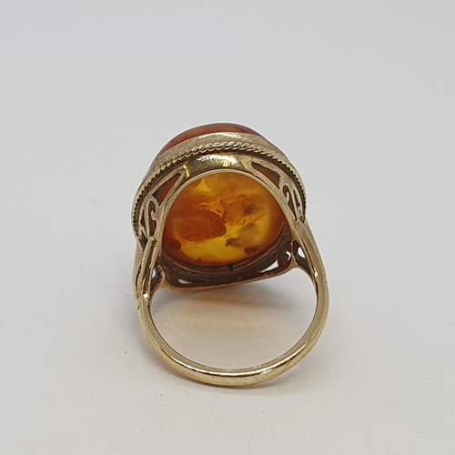 224 - An Amber Ring rubover set large cabochon in 9ct gold rope twist frame and split fleur de lys shoulde... 