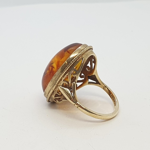 224 - An Amber Ring rubover set large cabochon in 9ct gold rope twist frame and split fleur de lys shoulde... 