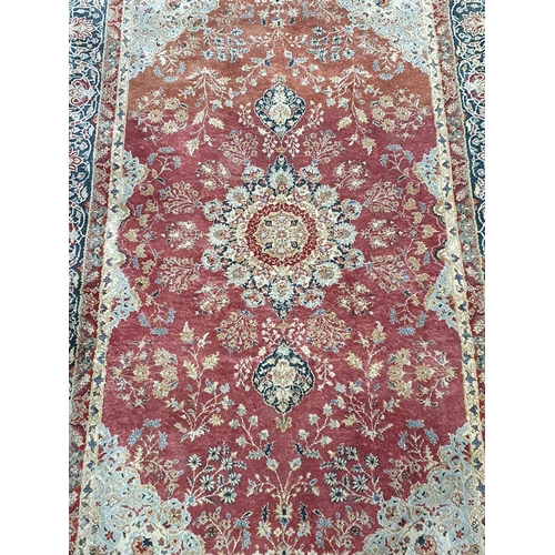 941 - A fine Persian style wool Rug with floral borders and central stylised flower head on a red ground, ... 