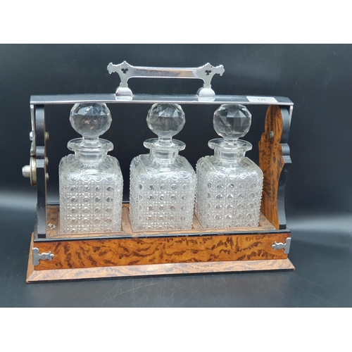 125 - A plated mounted Tantalus fitted three square cut glass decanters and stoppers, in stained and simul... 