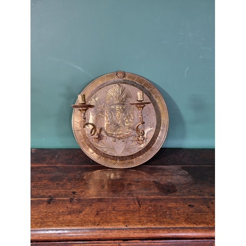 50 - A circular brass embossed Wall Sconce with Armorial Crest and leafage designs with a pair of swing c... 