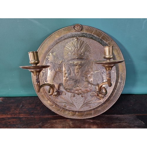 50 - A circular brass embossed Wall Sconce with Armorial Crest and leafage designs with a pair of swing c... 