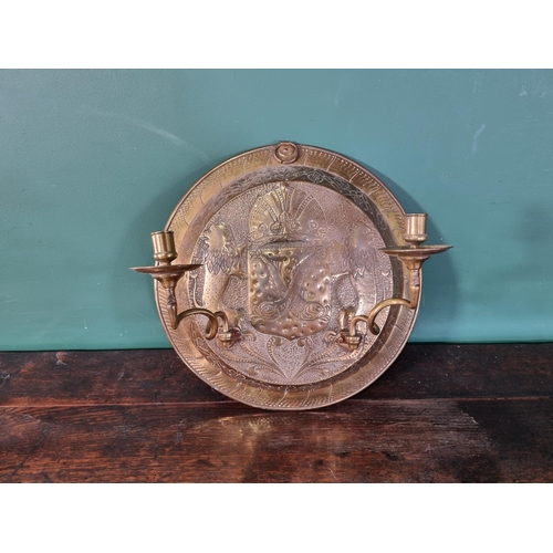 50 - A circular brass embossed Wall Sconce with Armorial Crest and leafage designs with a pair of swing c... 