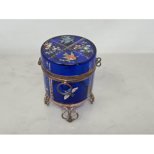 52 - A blue glass cylindrical Box with hinged lid enameled with birds and flowers, on metal scroll suppor... 