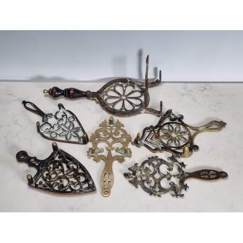 304 - Five assorted pierced Iron Trivets with shaped handles, and another with hearth stand and turned han... 