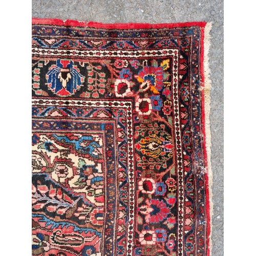 655 - A large Persian woollen Carpet with central cream diamond shaped flower head within red ground with ... 