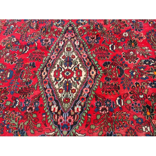 655 - A large Persian woollen Carpet with central cream diamond shaped flower head within red ground with ... 