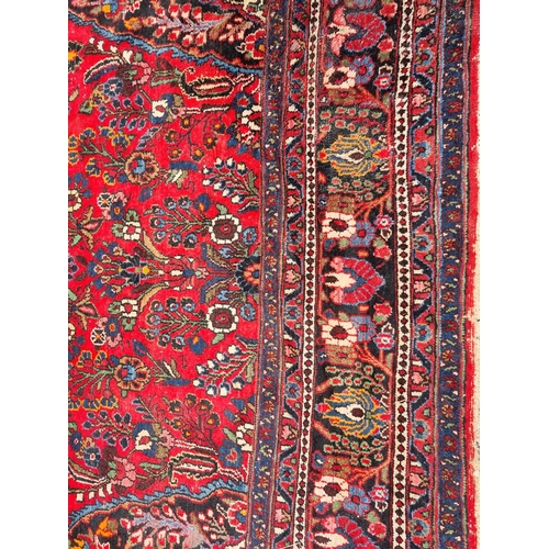 655 - A large Persian woollen Carpet with central cream diamond shaped flower head within red ground with ... 