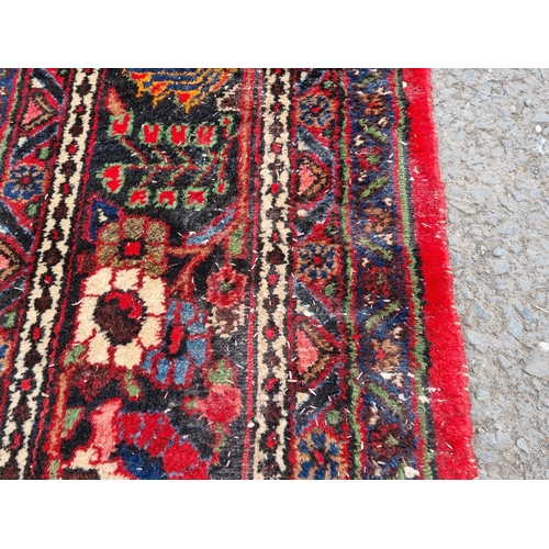 655 - A large Persian woollen Carpet with central cream diamond shaped flower head within red ground with ... 