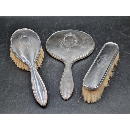 155 - A George V silver mounted Mirror and two Brushes engraved oval leafage cartouches, Birmingham 1915 &... 