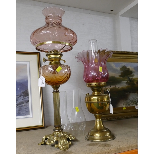 208 - Two brass duplex oil lamps with pink shades, one with glass reservoir, and two spare chimneys