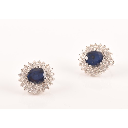 64 - A pair of 14ct white gold, diamond, and sapphire cluster earrings, each set with a mixed oval-cut sa... 