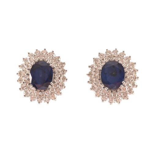 64 - A pair of 14ct white gold, diamond, and sapphire cluster earrings, each set with a mixed oval-cut sa... 