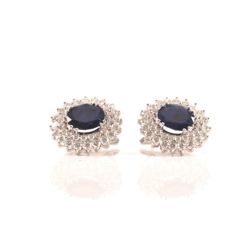 64 - A pair of 14ct white gold, diamond, and sapphire cluster earrings, each set with a mixed oval-cut sa... 