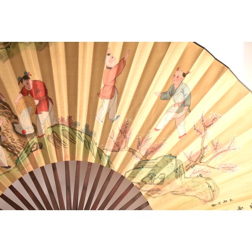 246 - A very large Chinese painted decorative display fan, painted with a scene of children playing by a t... 