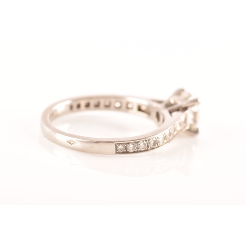 8 - Cartier. A platinum diamond flanked solitaire ring, set with a round brilliant cut diamond with an a... 