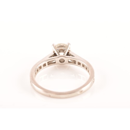 8 - Cartier. A platinum diamond flanked solitaire ring, set with a round brilliant cut diamond with an a... 