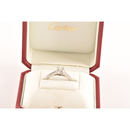 8 - Cartier. A platinum diamond flanked solitaire ring, set with a round brilliant cut diamond with an a... 