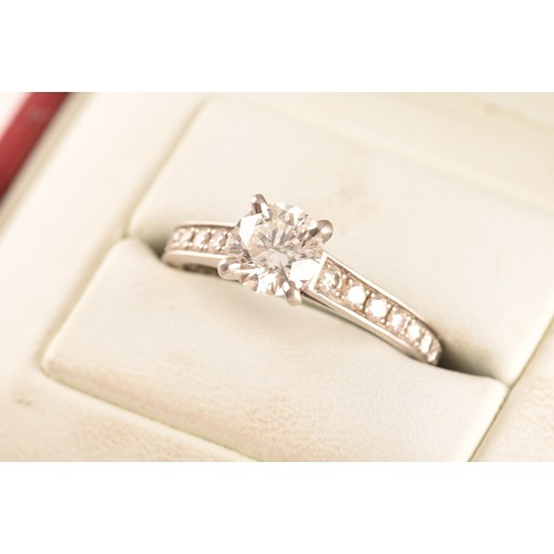 8 - Cartier. A platinum diamond flanked solitaire ring, set with a round brilliant cut diamond with an a... 