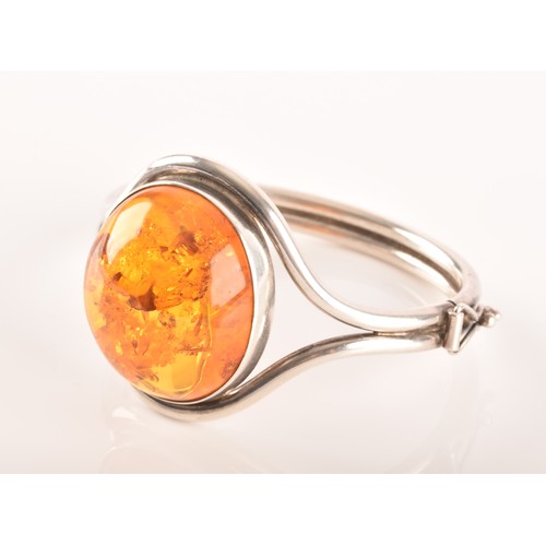 92 - A silver and amber bangle bracelet, set with a large oval cabochon amber, measuring approximately 3.... 