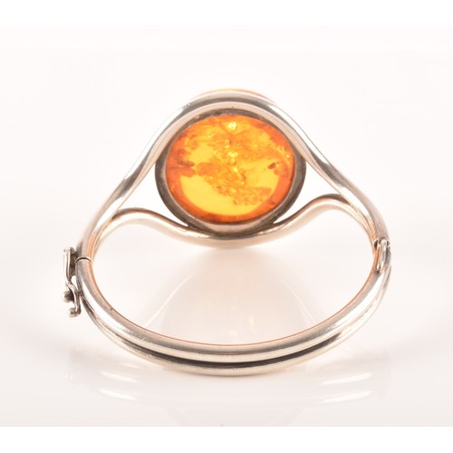 92 - A silver and amber bangle bracelet, set with a large oval cabochon amber, measuring approximately 3.... 