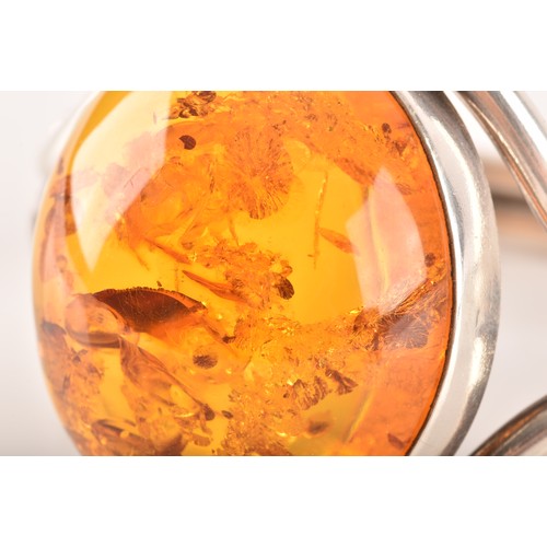 92 - A silver and amber bangle bracelet, set with a large oval cabochon amber, measuring approximately 3.... 