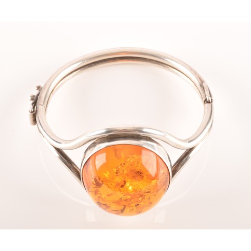 92 - A silver and amber bangle bracelet, set with a large oval cabochon amber, measuring approximately 3.... 