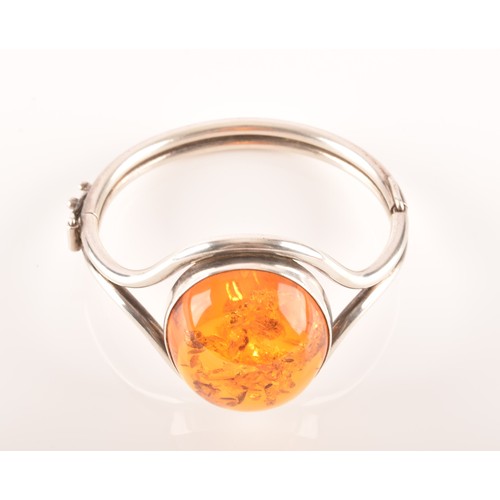 92 - A silver and amber bangle bracelet, set with a large oval cabochon amber, measuring approximately 3.... 