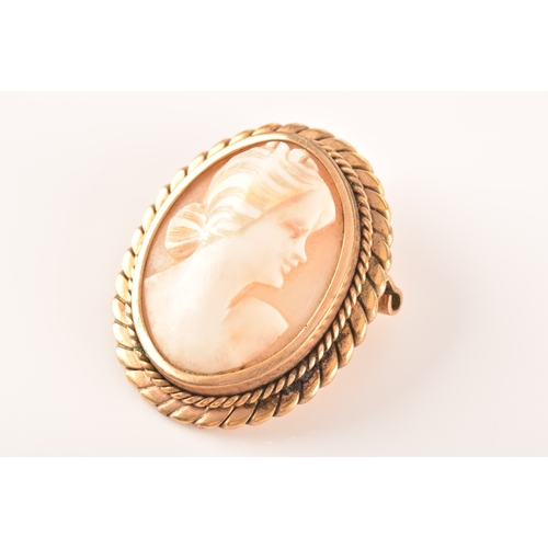 68 - A yellow metal mounted cameo brooch, the cameo depicting a woman in a long dress standing in a rural... 