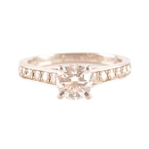 8 - Cartier. A platinum diamond flanked solitaire ring, set with a round brilliant cut diamond with an a... 