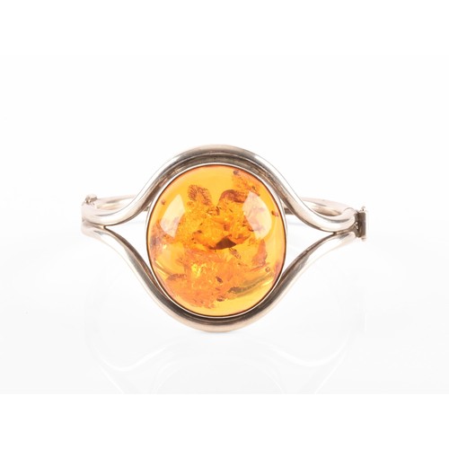 92 - A silver and amber bangle bracelet, set with a large oval cabochon amber, measuring approximately 3.... 