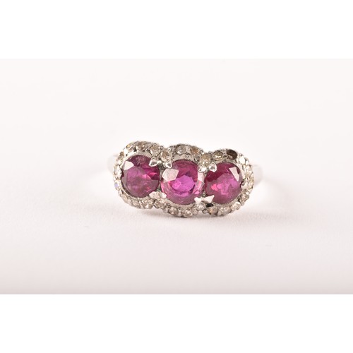 102 - A early 20th century white metal cluster ring, featuring three round old cut rubies with a combined ... 