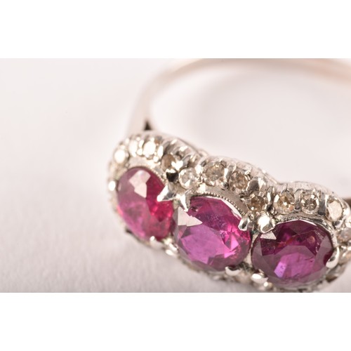 102 - A early 20th century white metal cluster ring, featuring three round old cut rubies with a combined ... 