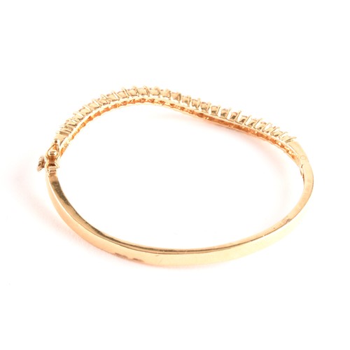 137 - A yellow gold and diamond bangle, of waved design, set with twenty-five round brilliant-cut diamonds... 