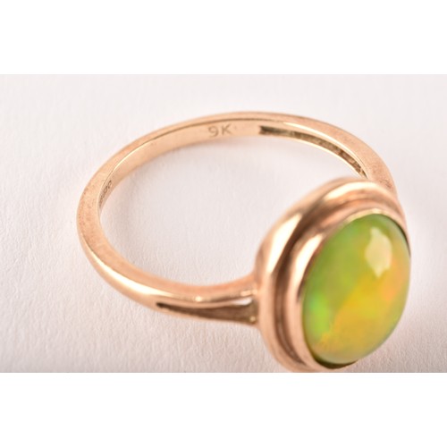 154 - An unusual 9ct yellow gold and opal ring, the oval cabochon opal showing strong green and orange pla... 