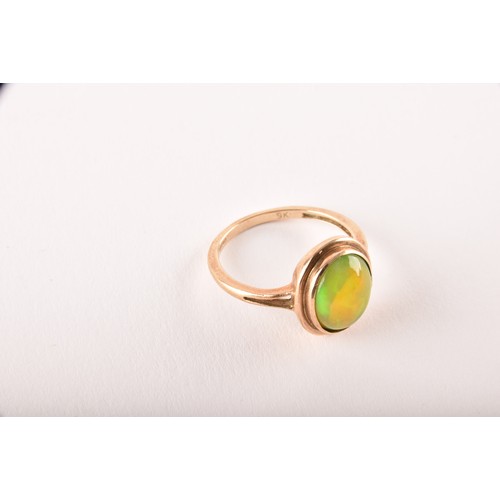 154 - An unusual 9ct yellow gold and opal ring, the oval cabochon opal showing strong green and orange pla... 