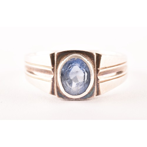 157 - A silver and sapphire gents ring, bezel-set with a mixed oval-cut sapphire, the mount with stylised ... 