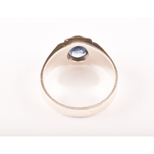 157 - A silver and sapphire gents ring, bezel-set with a mixed oval-cut sapphire, the mount with stylised ... 