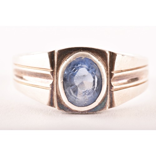 157 - A silver and sapphire gents ring, bezel-set with a mixed oval-cut sapphire, the mount with stylised ... 