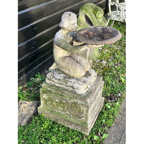 205 - An early 20th century carved and painted stone bird bath, modelled as a nude girl holding aloft a di... 