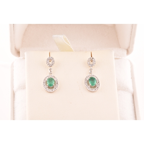 53 - A pair of 18ct white gold emerald and diamond drop earrings, each set with an oval cut emerald with ... 