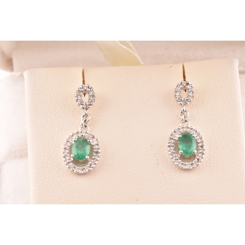 53 - A pair of 18ct white gold emerald and diamond drop earrings, each set with an oval cut emerald with ... 